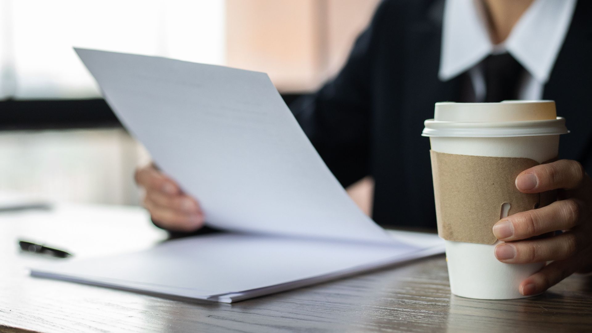 Focused businesswoman examining documents with a disposable coffee cup on a wooden desk.