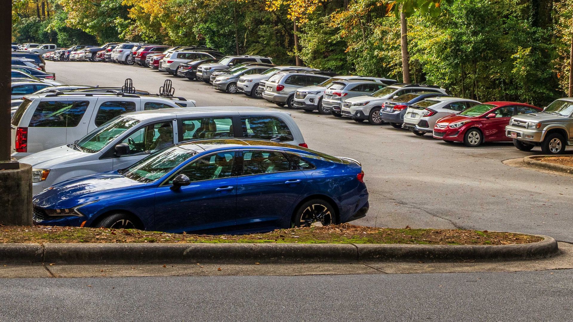 Scenic autumn parking lot with colorful trees and parked cars under a cloudy sky.