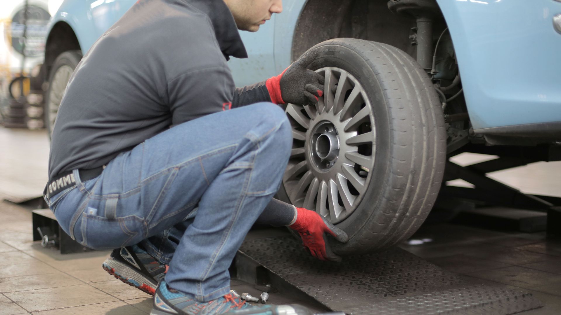 Mechanic changing a car tire indoors, using tools for vehicle maintenance.
