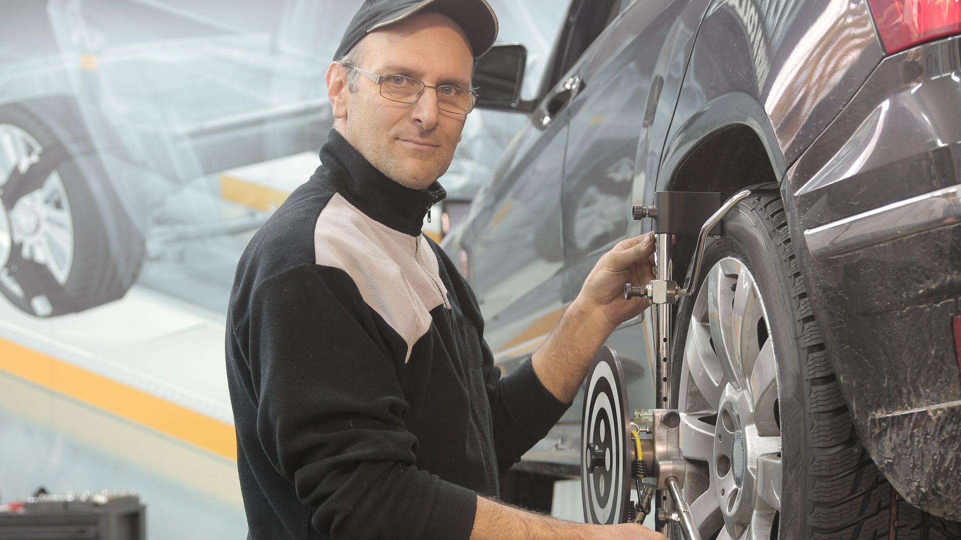 Mechanic performing wheel alignment on a car in a professional garage setting.