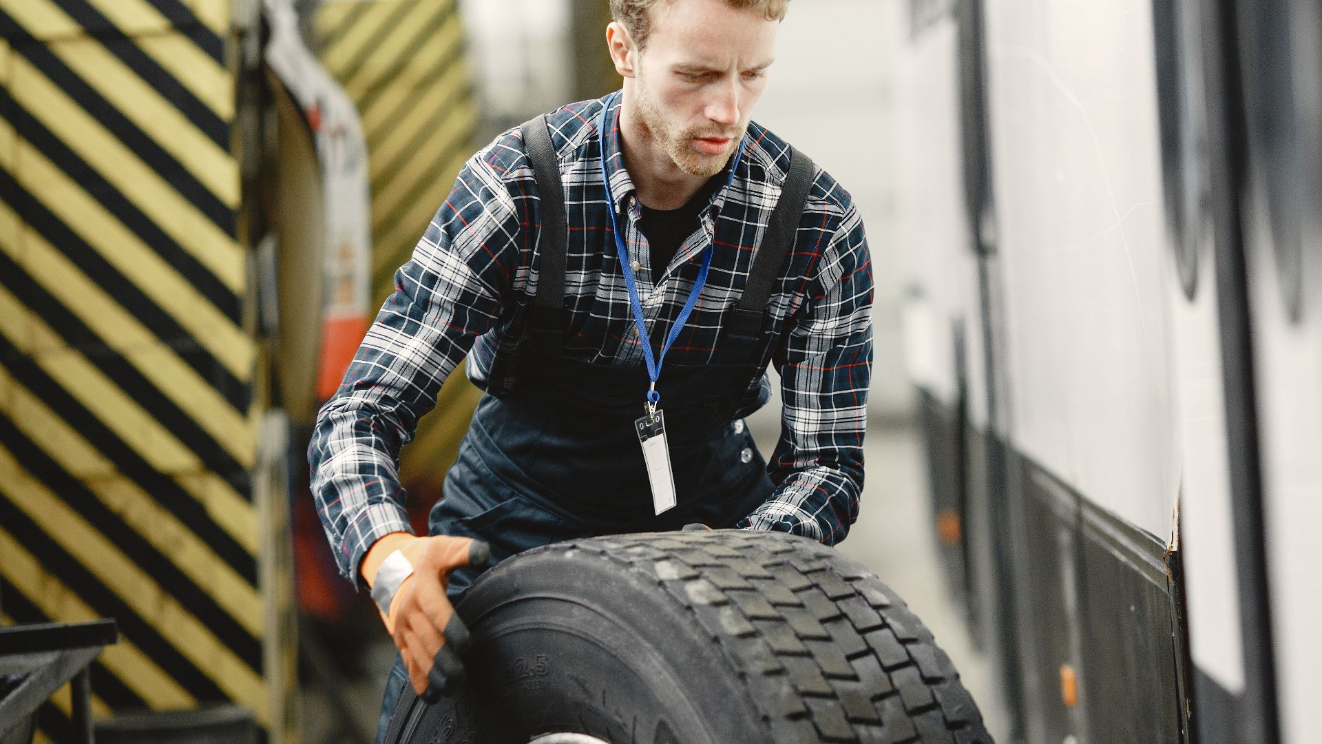 Auto mechanic working indoors in a vehicle repair garage managing a large tire.