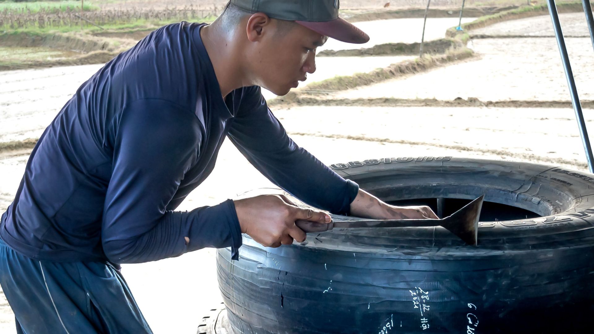 Mechanic fixing tires in an outdoor garage near a rural landscape.