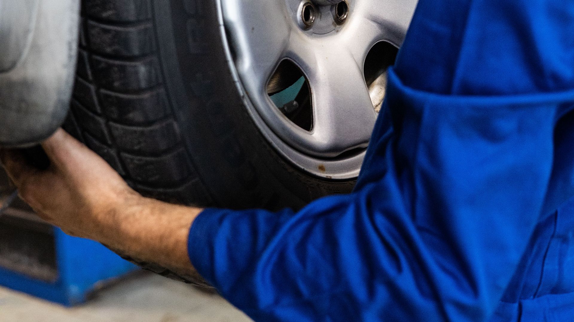 A mechanic in blue uniform closely examines a car wheel for repairs.