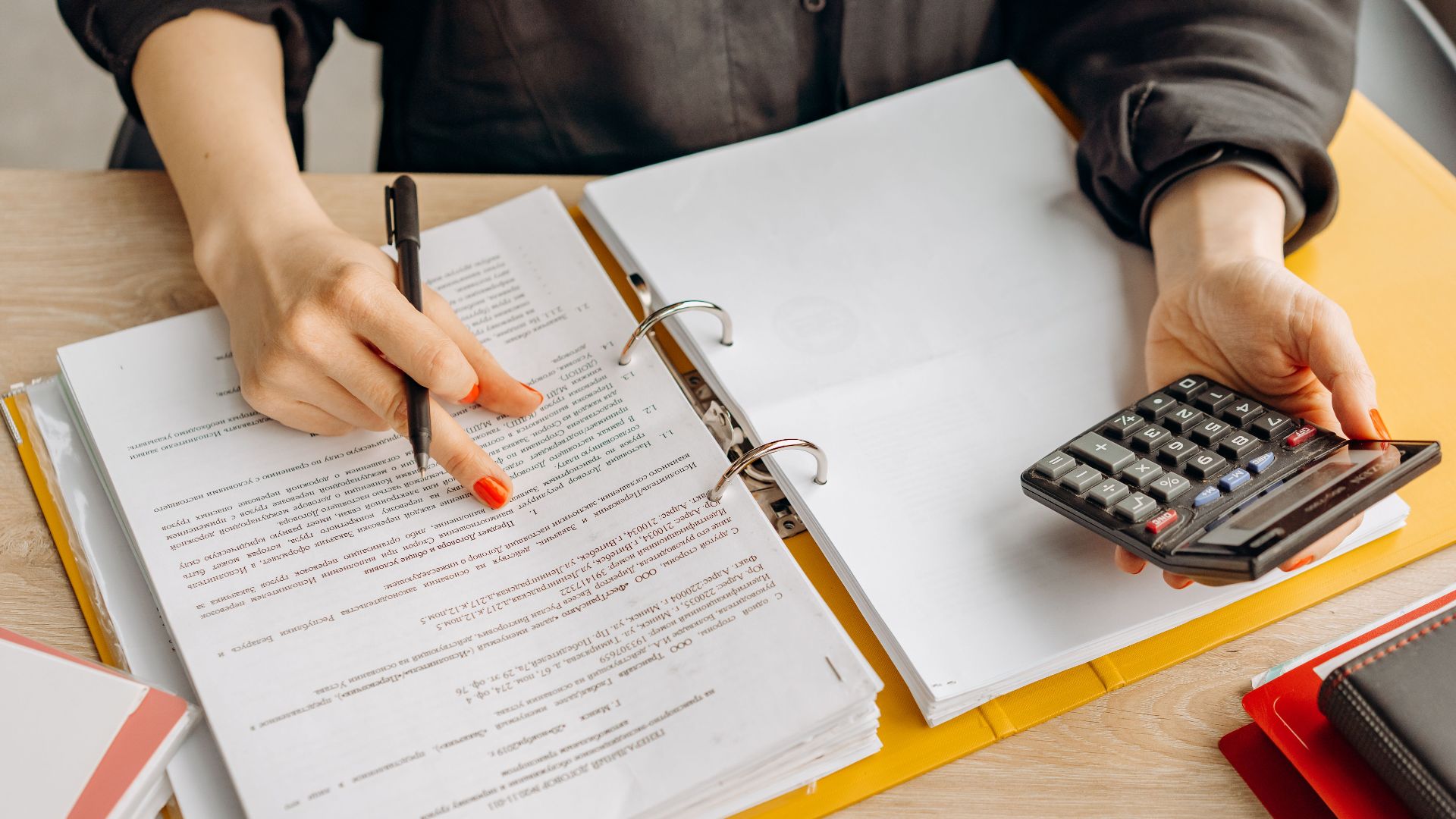 A woman reviewing documents and using a calculator on a wooden table.