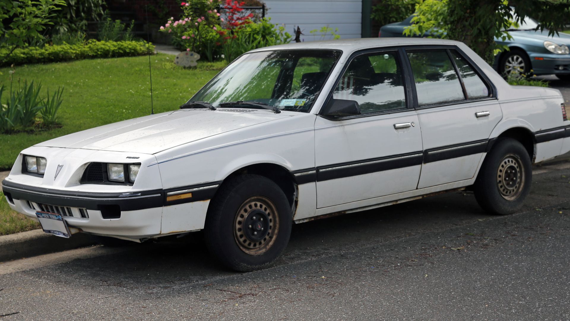 A 1986 Pontiac Sunbird, base four-door with the Brazilian-built, 84hp 1.8 with throttle-body fuel injection (LH8). Assembled in Lordstown, Ohio. Massive surface rust, removed with photoshop.