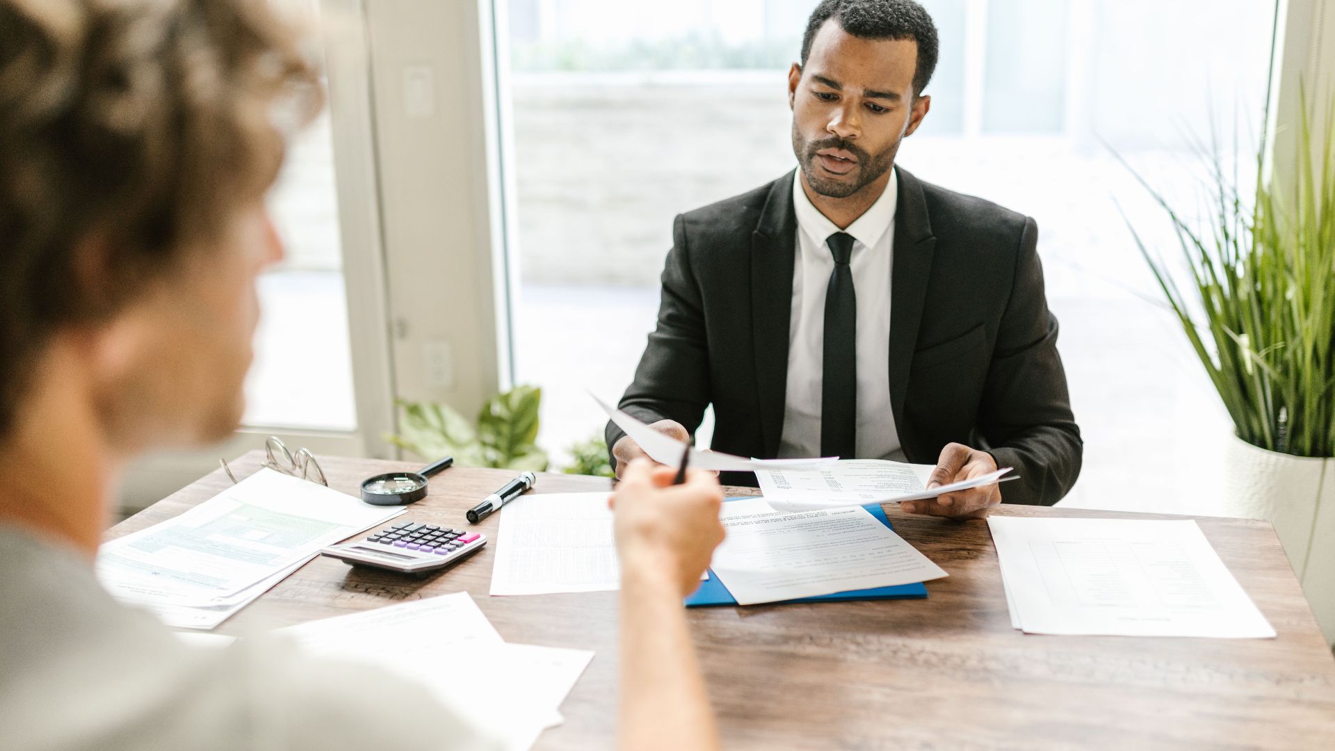 Businessman in a suit reviewing documents during a meeting indoors with a colleague.