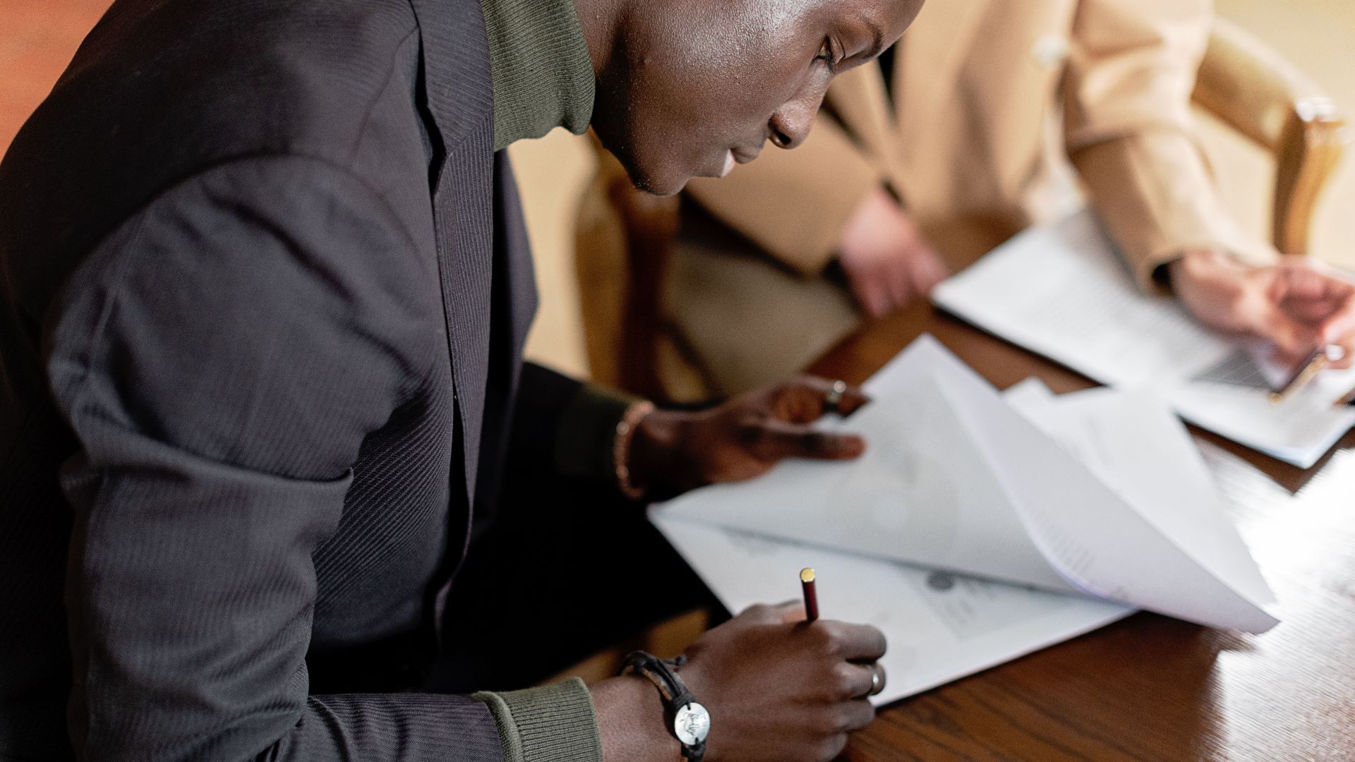 African American man focused on signing important business documents at a desk.