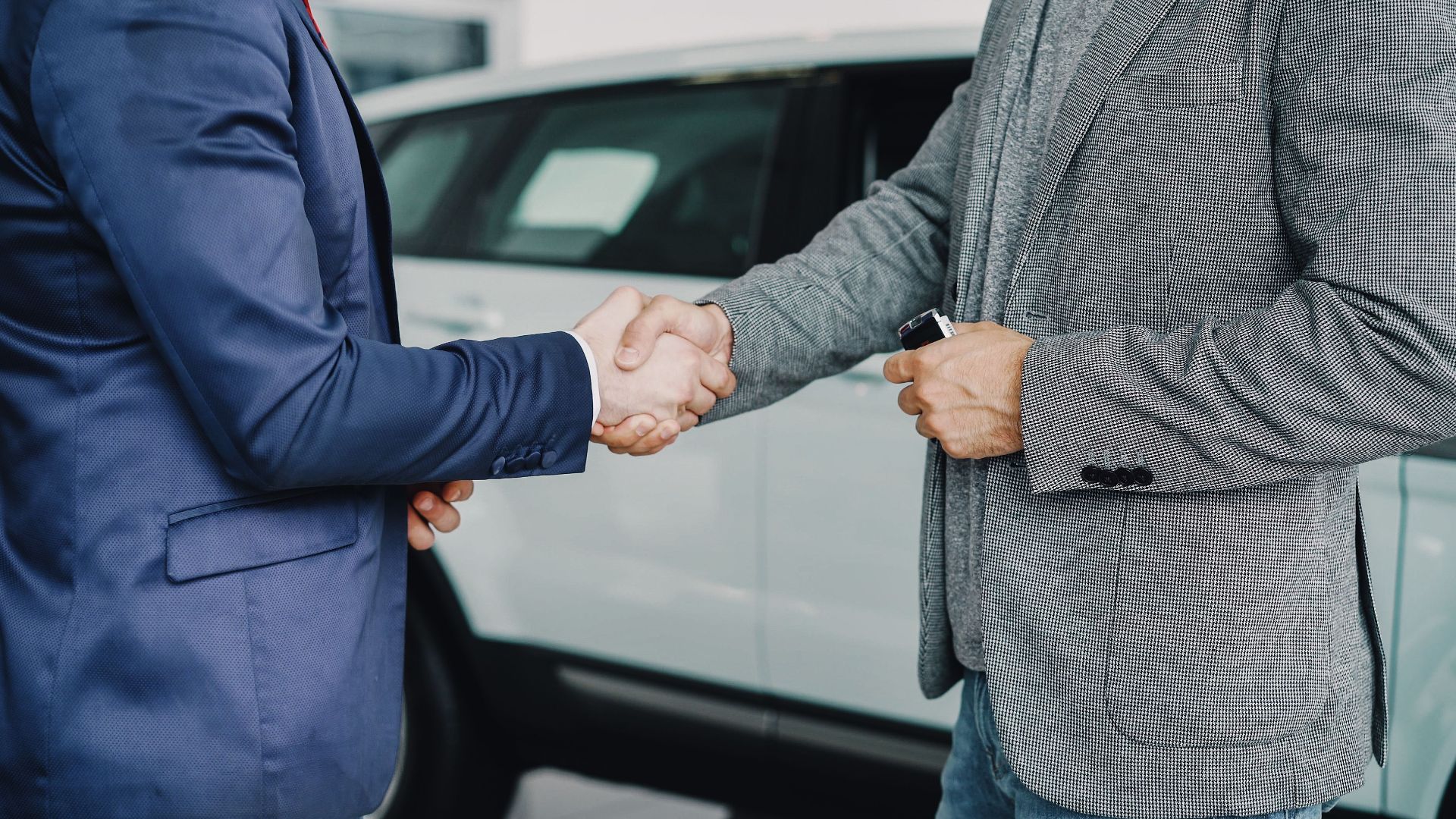 Two businessmen shaking hands in a car dealership, sealing a deal.