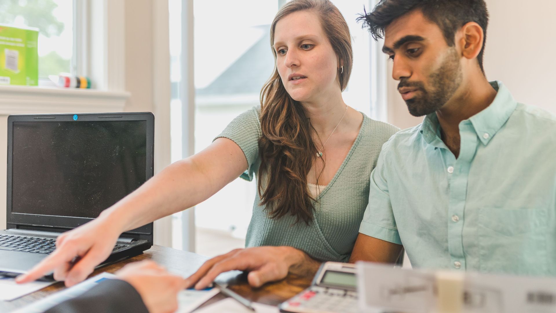 A young couple reviewing real estate documents with an advisor in a bright office.