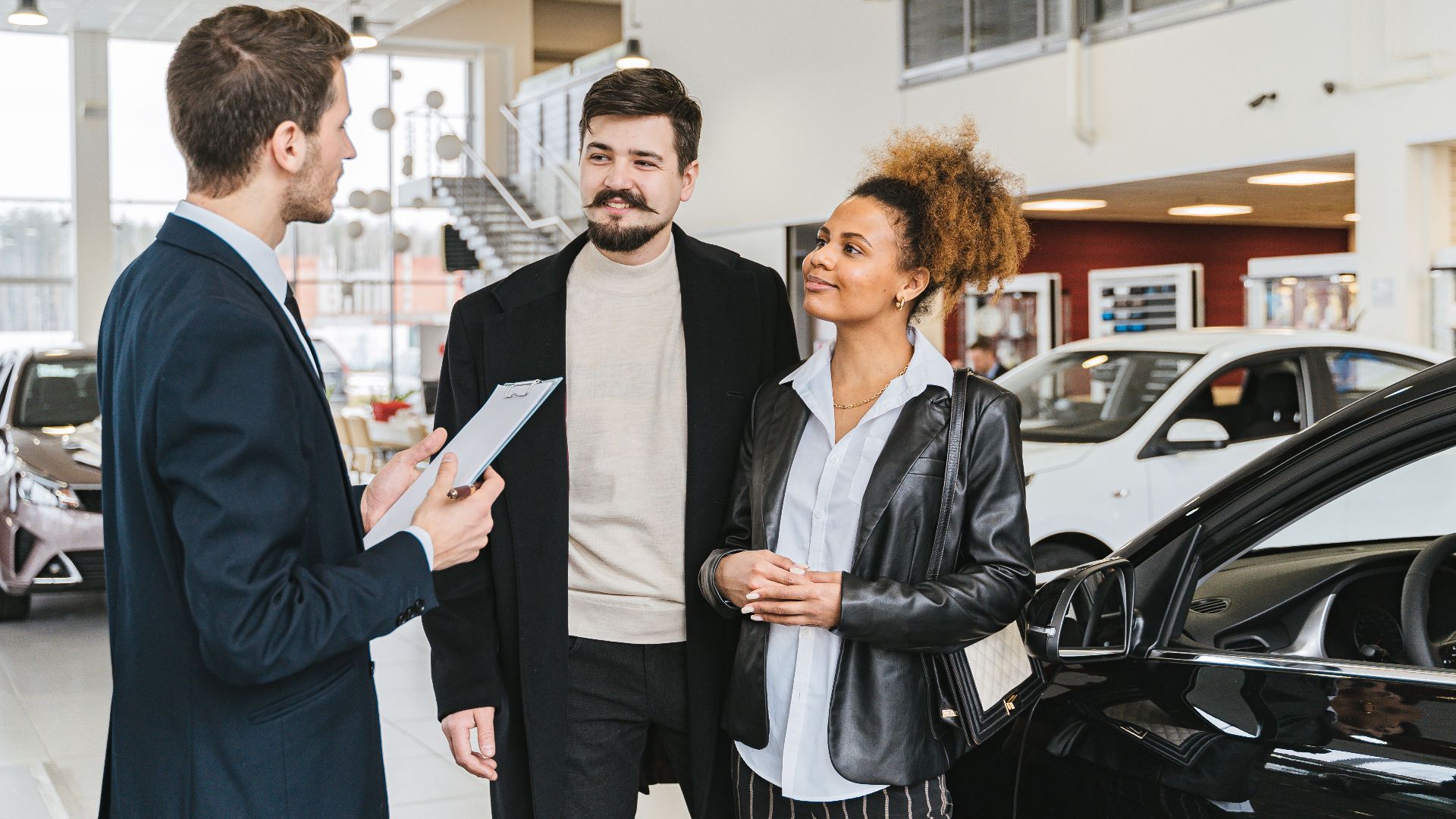 Couple discussing car purchase with salesman at indoor dealership, engaging conversation.