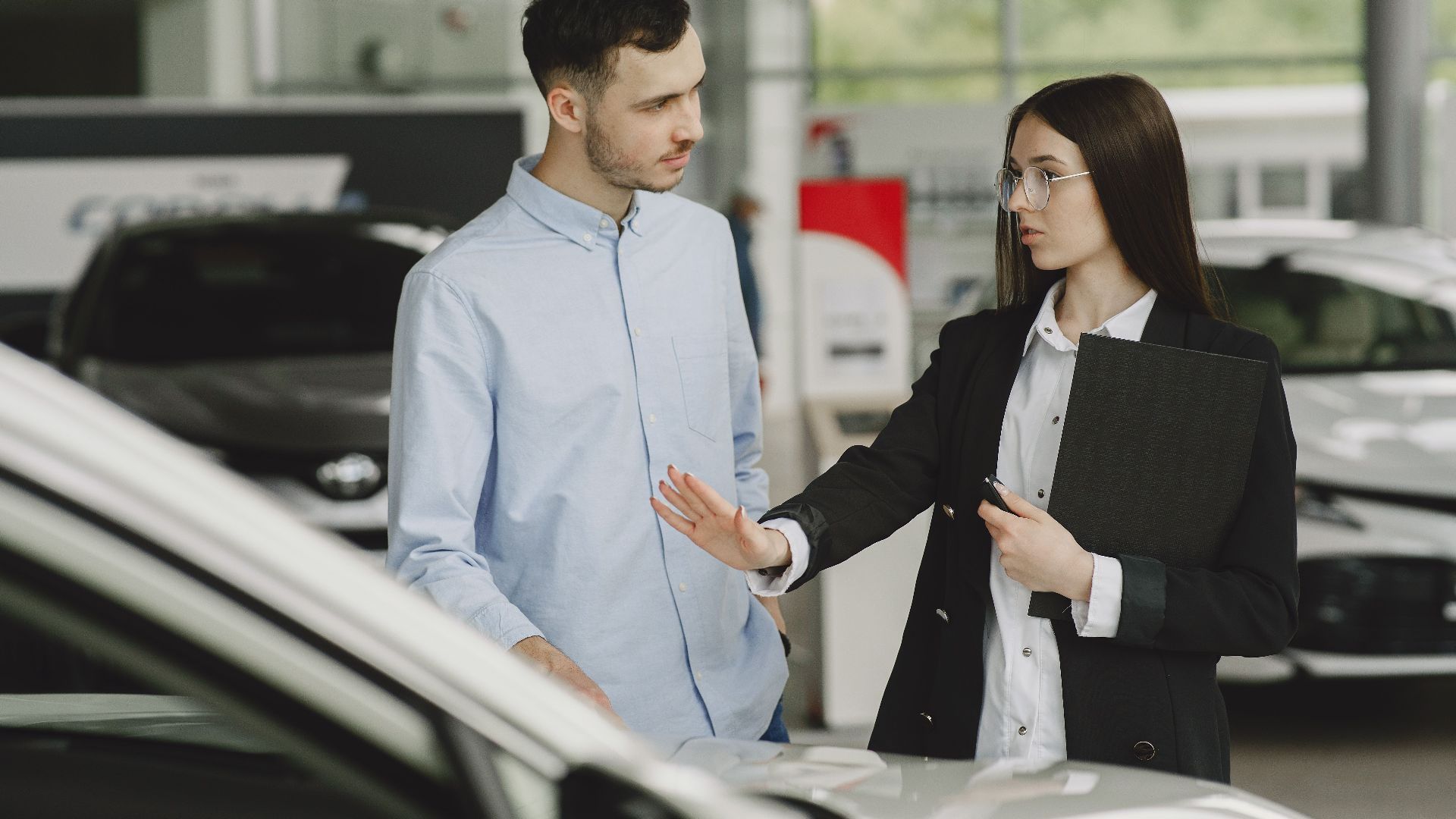 A salesperson and customer discussing car features in a dealership setting.