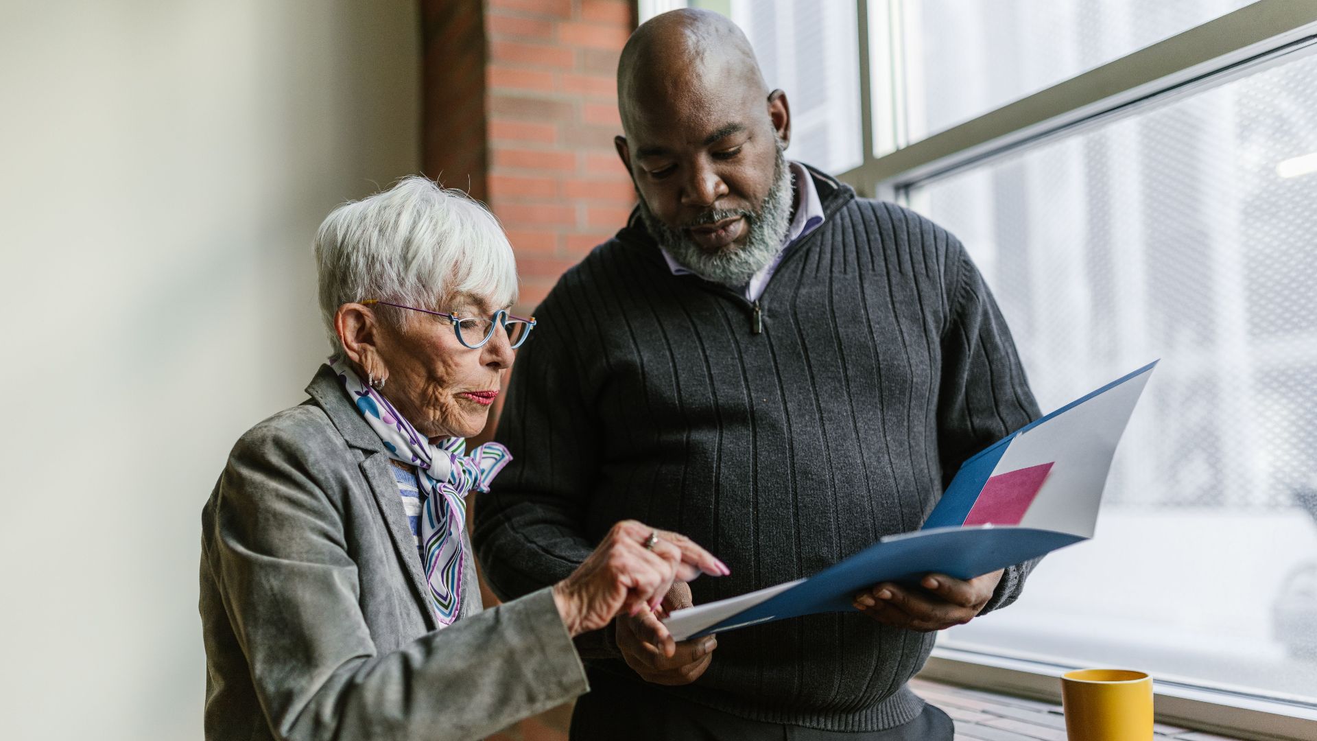 Senior colleagues working together, reviewing documents near an office window.