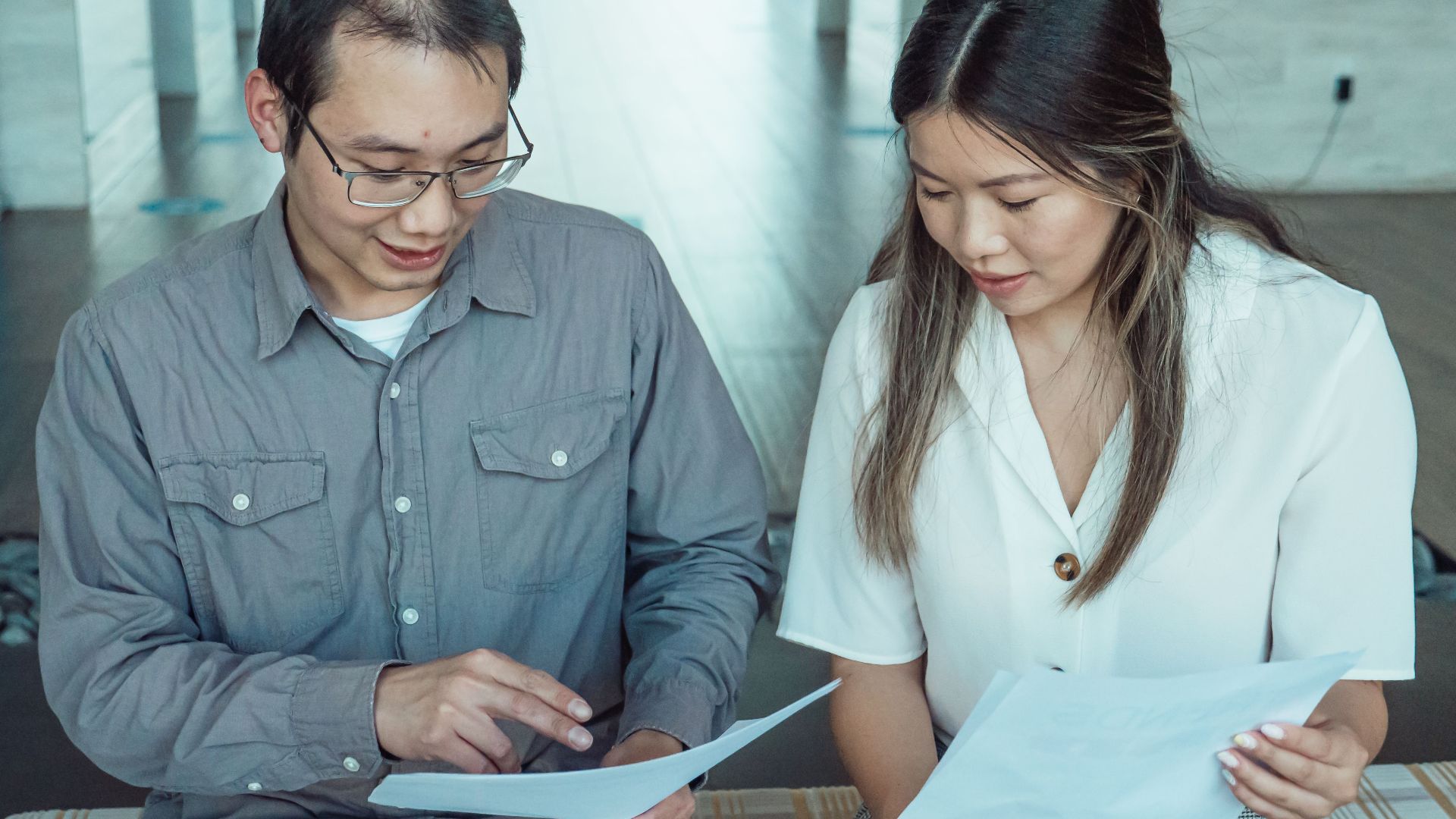 Two coworkers reviewing documents in a modern office, focused on teamwork and planning.