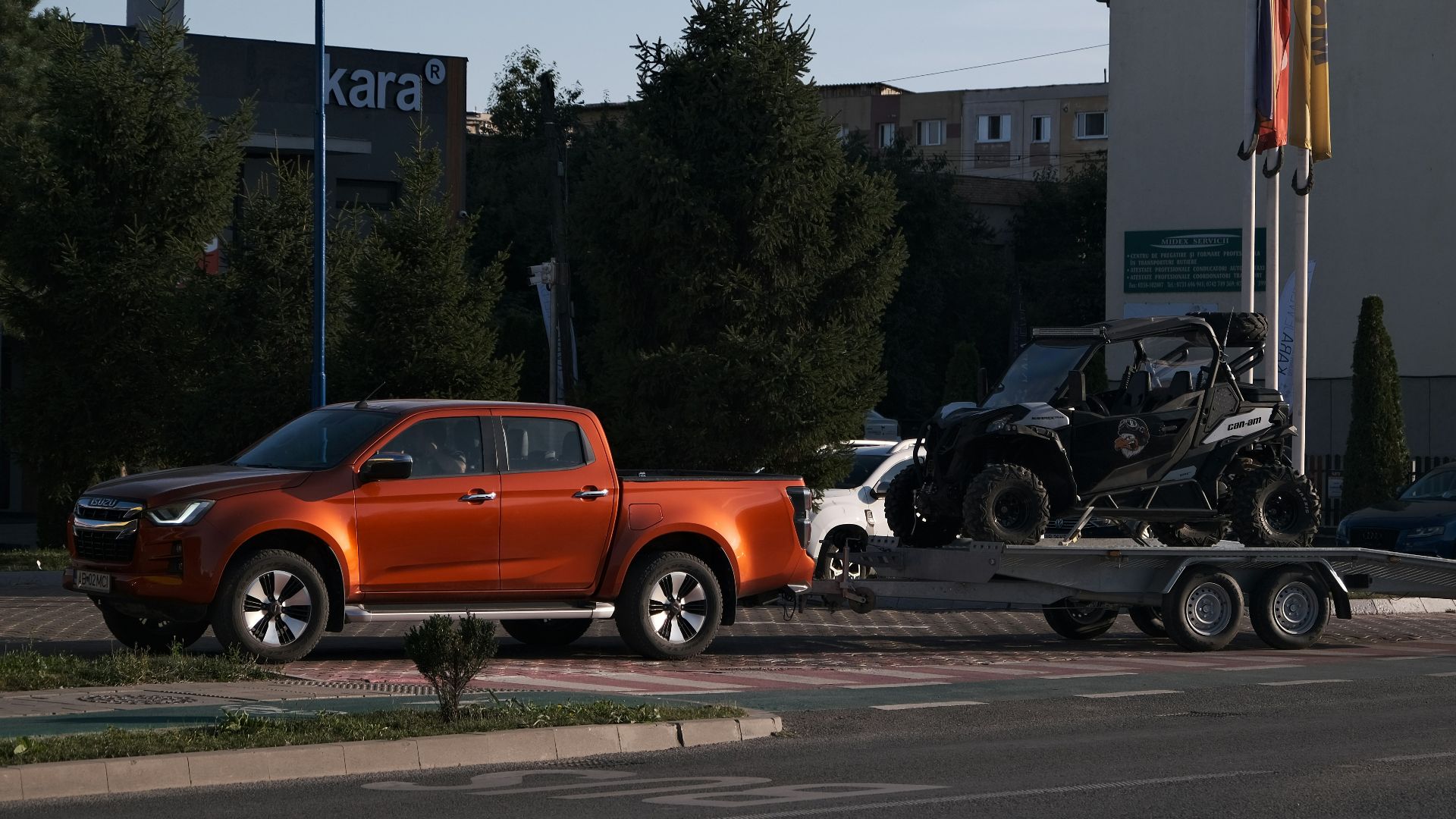An orange pickup truck towing a black off-road vehicle on a trailer