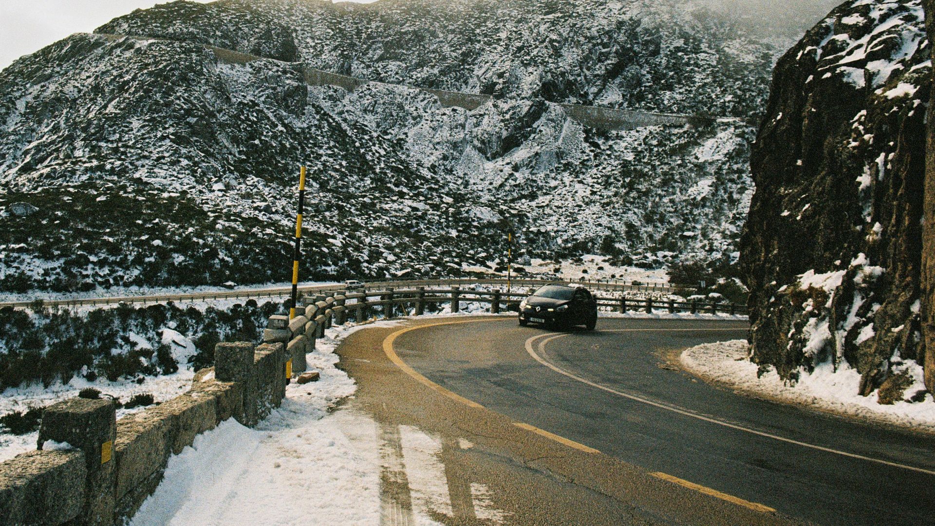 A car drives on a winding mountain road in winter