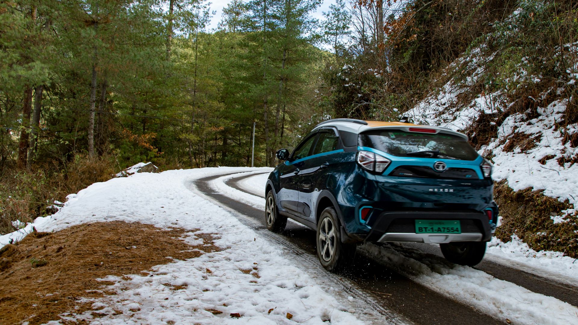 a blue car driving down a snowy road