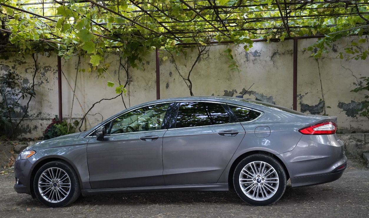 Side view of a silver sedan parked under a pergola with lush greenery