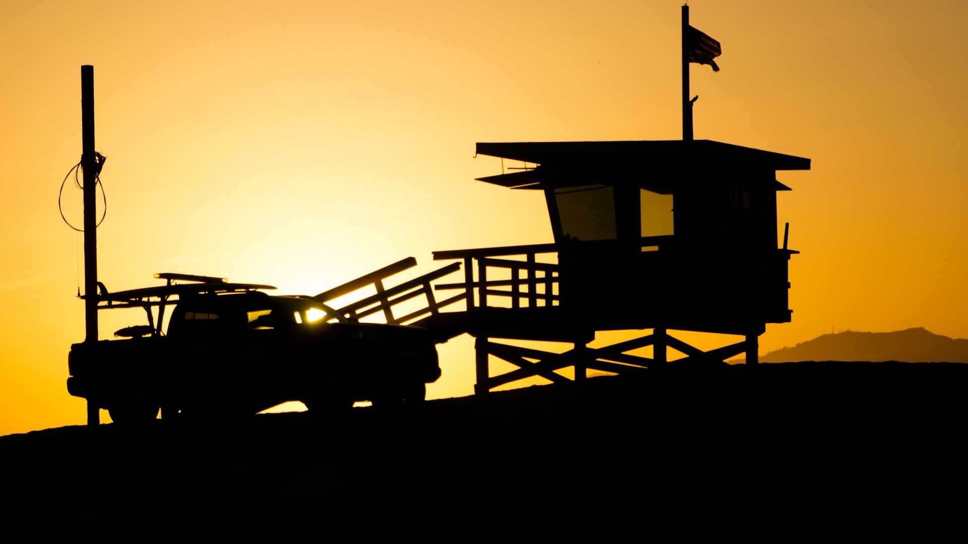 Silhouettes of people walking by a lifeguard hut during a golden sunset on the beach.