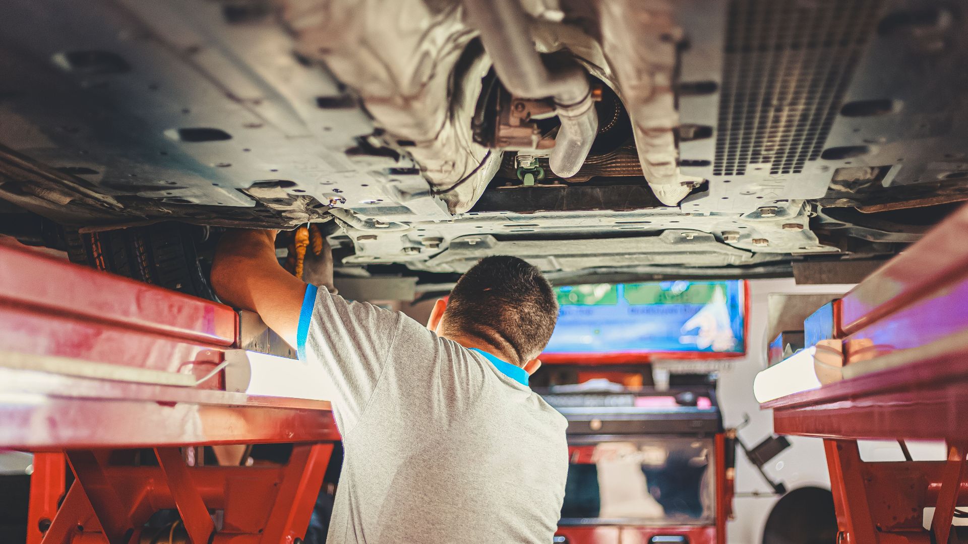 A mechanic works under a lifted car in an auto repair shop, adjusting parts.