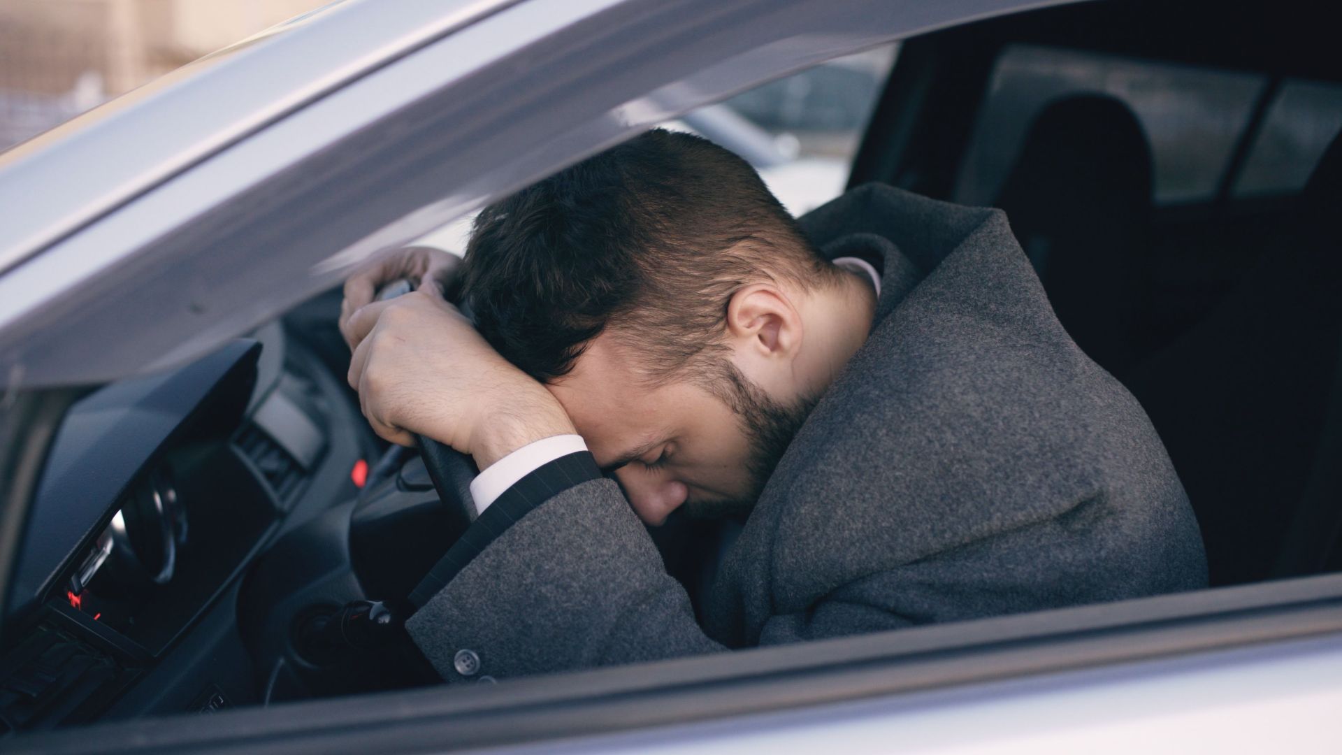 Man in car showing stress with head on steering wheel, highlighting emotional fatigue.