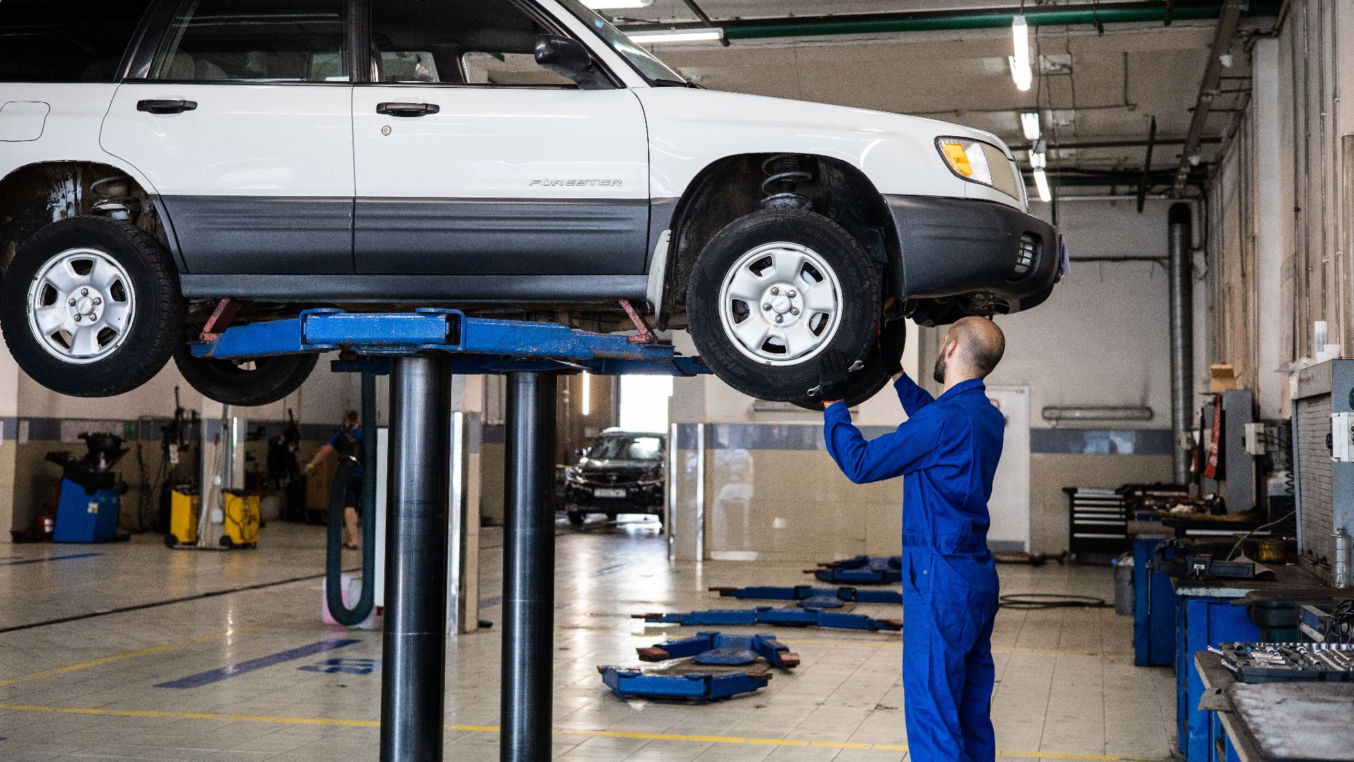 A mechanic inspecting a white SUV lifted in a well-lit auto repair shop.
