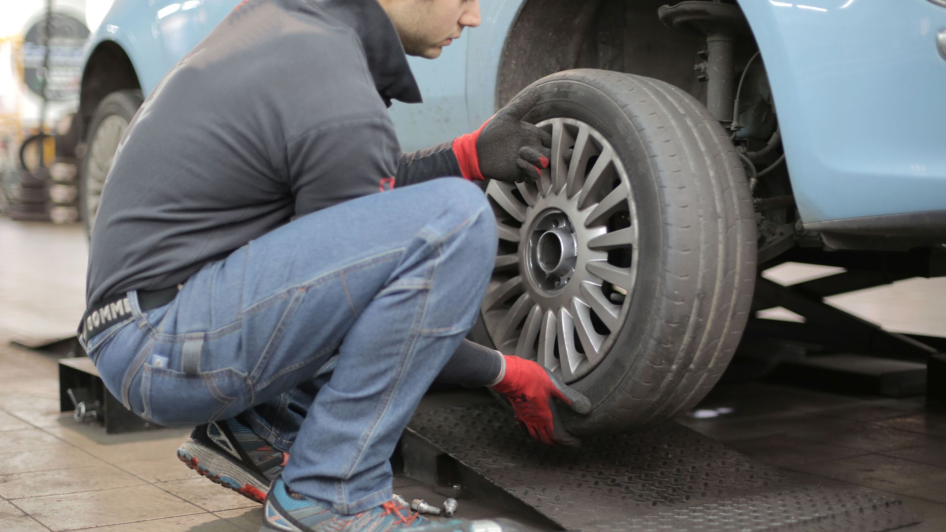 Mechanic changing a car tire indoors, using tools for vehicle maintenance.
