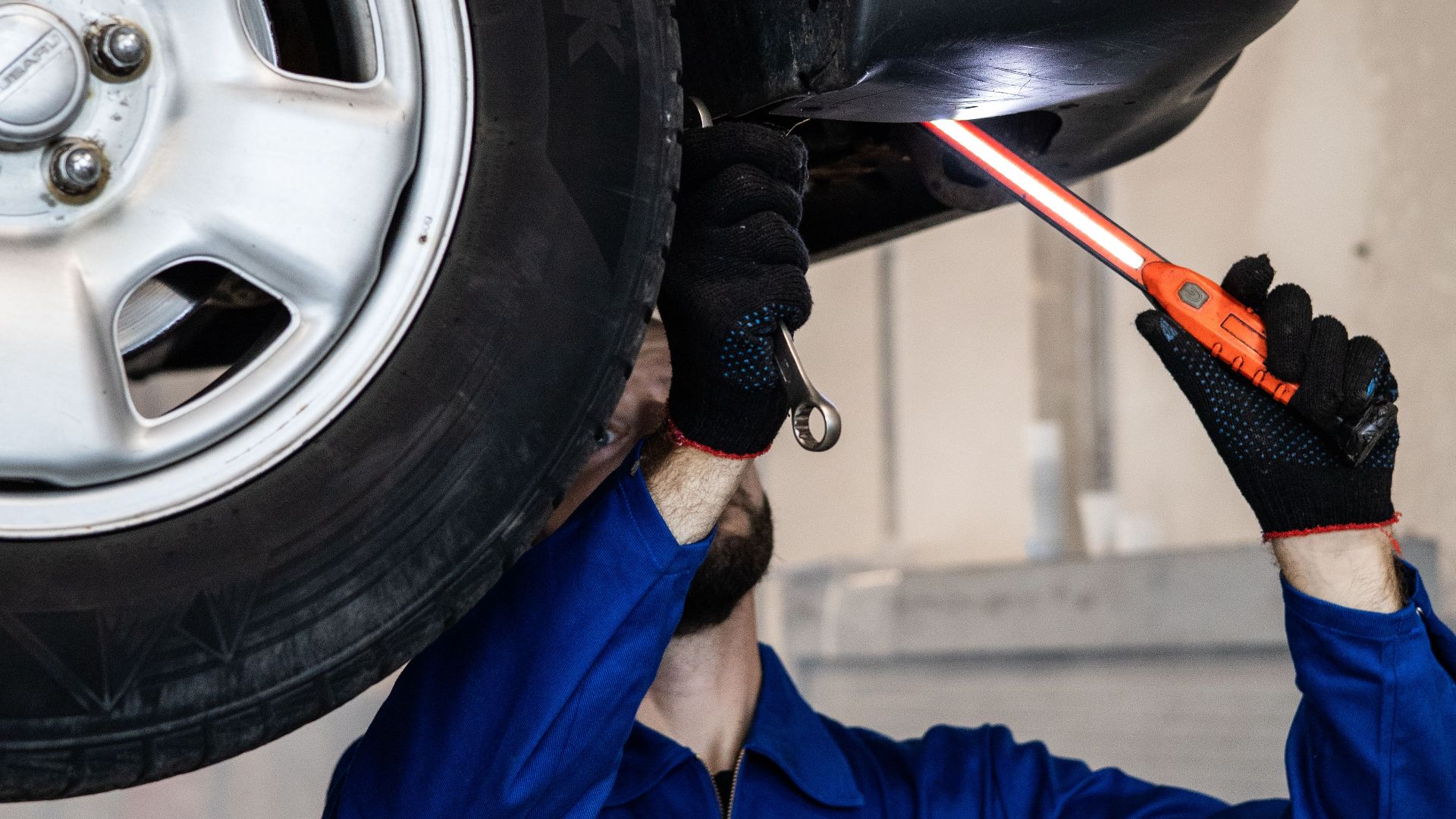 Mechanic inspecting a car in an auto repair shop, checking under the vehicle with a flashlight.