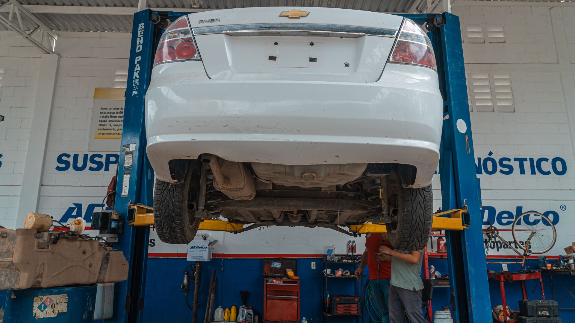 A white Chevrolet car is lifted for maintenance in an automotive repair shop.