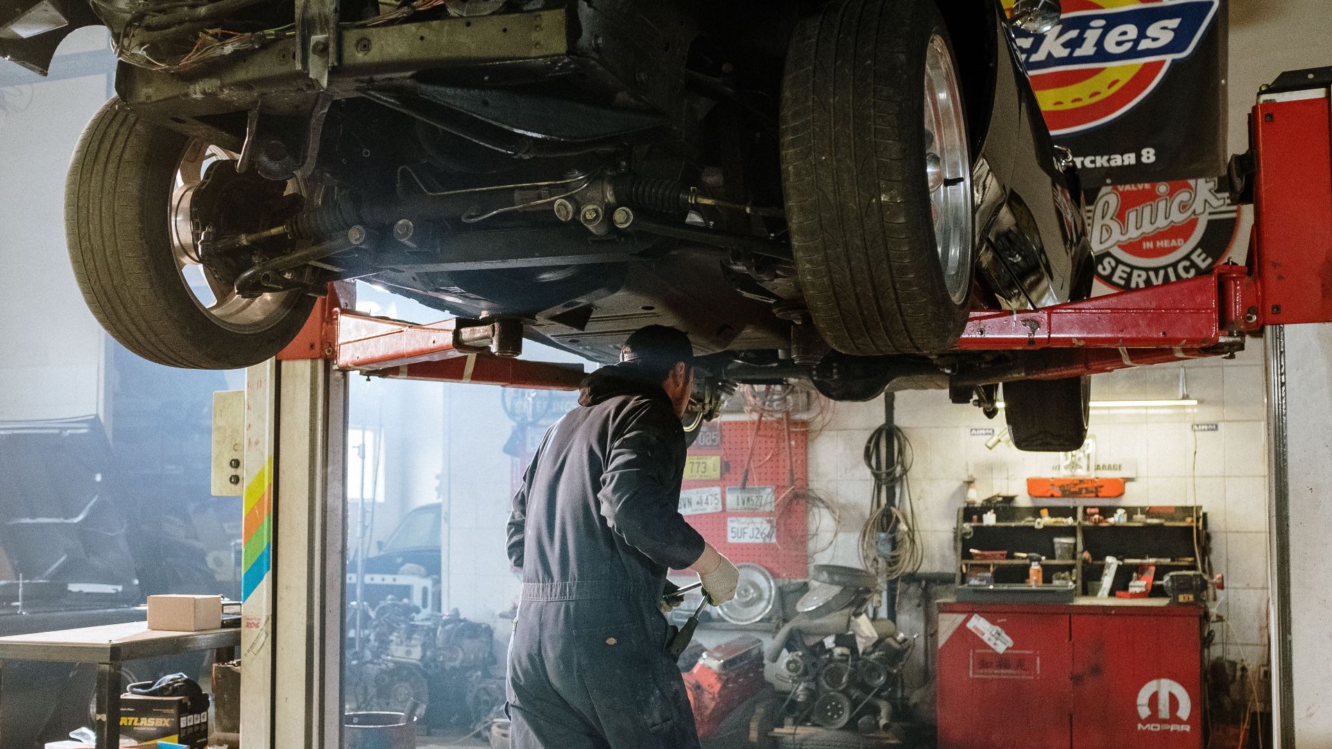 Mechanic repairing a vehicle in a busy workshop with various automotive tools.