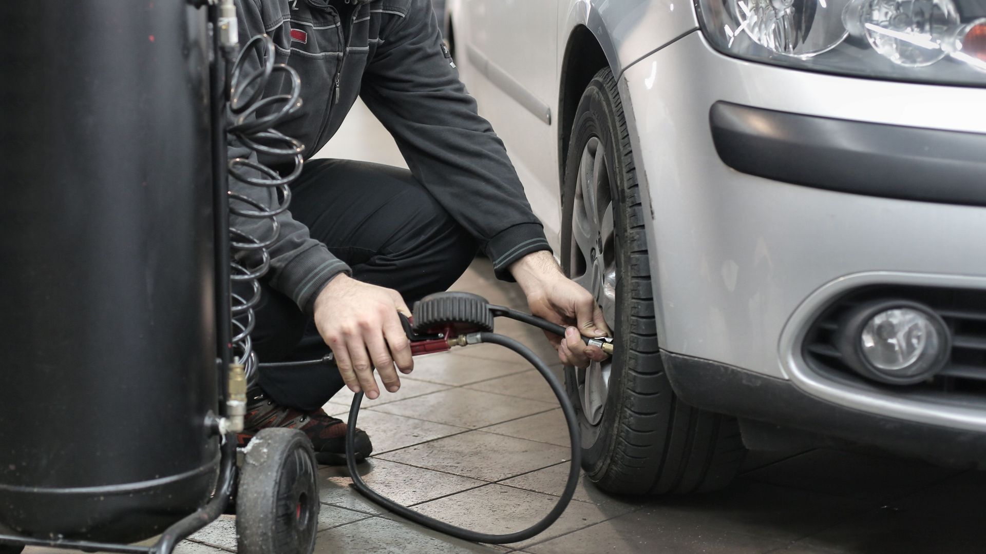 Mechanic inspecting and adjusting tire pressure in an auto repair shop.