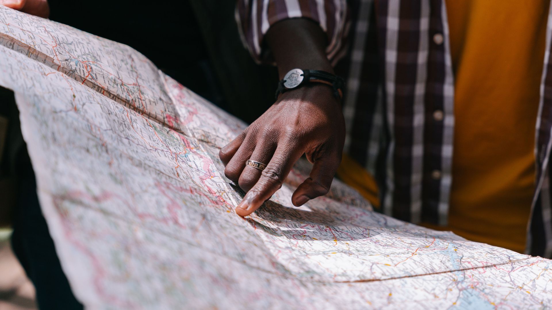 Close-up of a hand pointing at a detailed map, outdoors, wearing a striped shirt.
