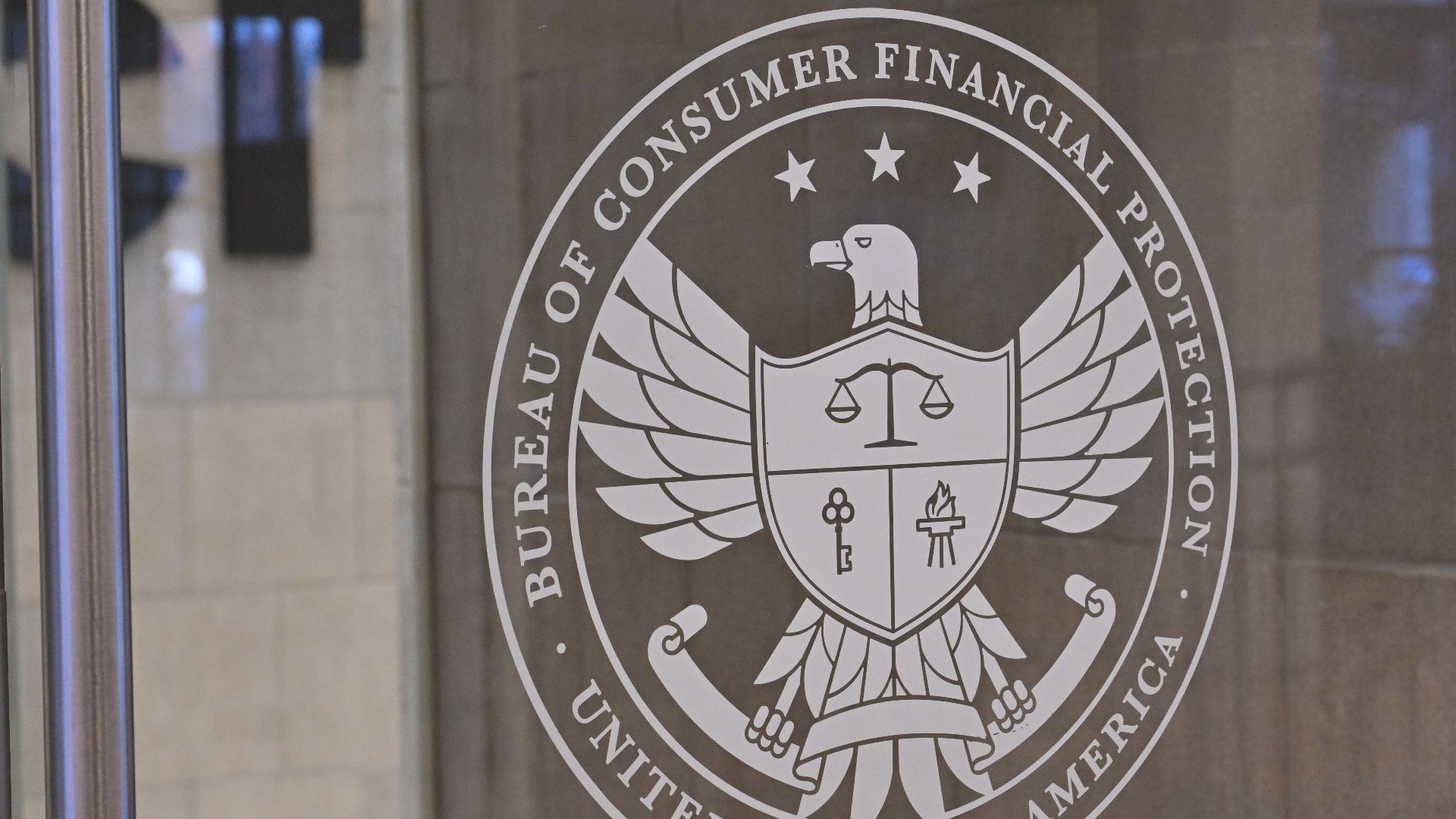 The logo for the Consumer Financial Protection Bureau on a glass door. 1700 G Street NW, Washington, DC 20552.