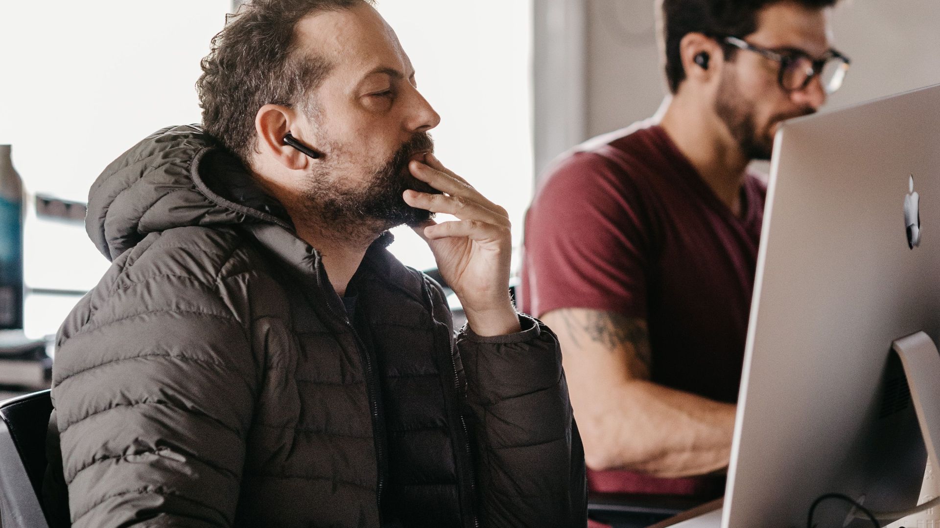 Two male office workers concentrating on their desktop computers in a modern workspace.