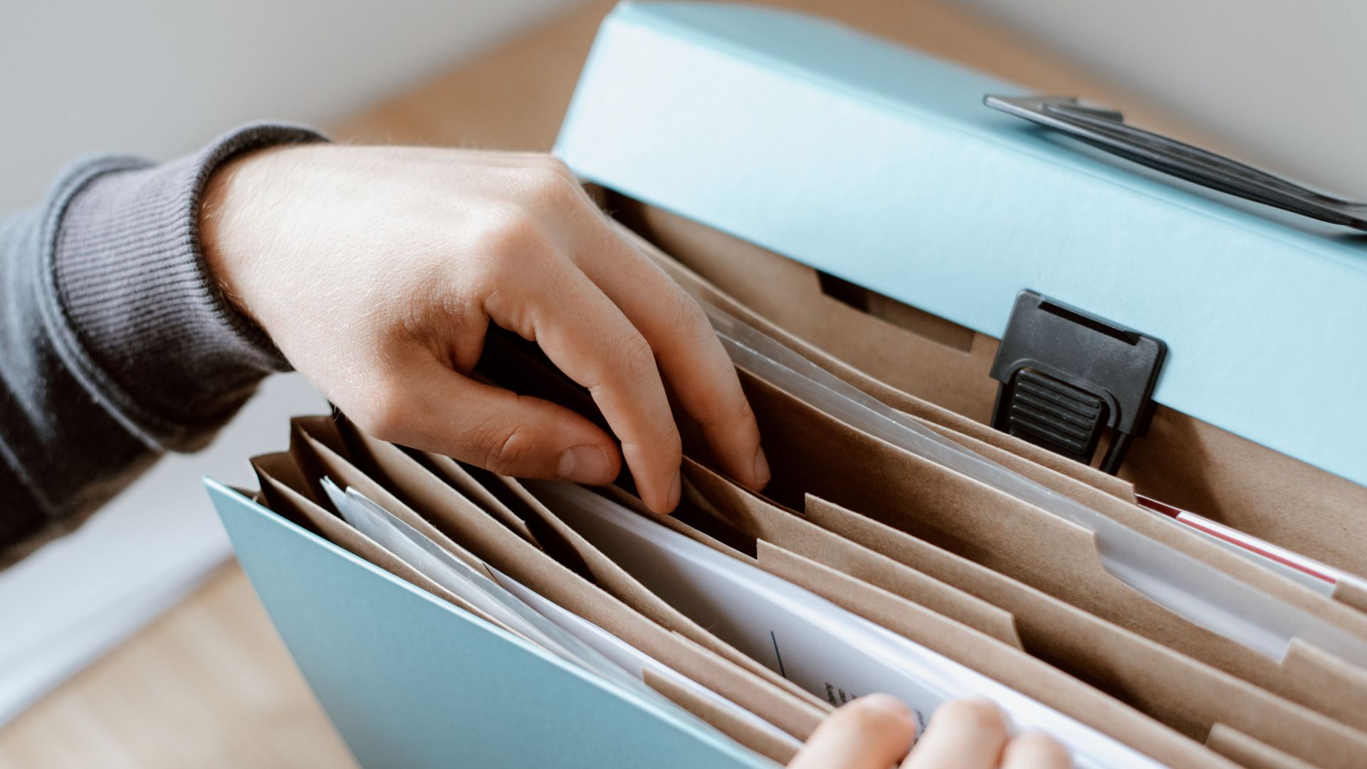 Crop unrecognizable person selecting document in opened briefcase for documents placed on wooden table