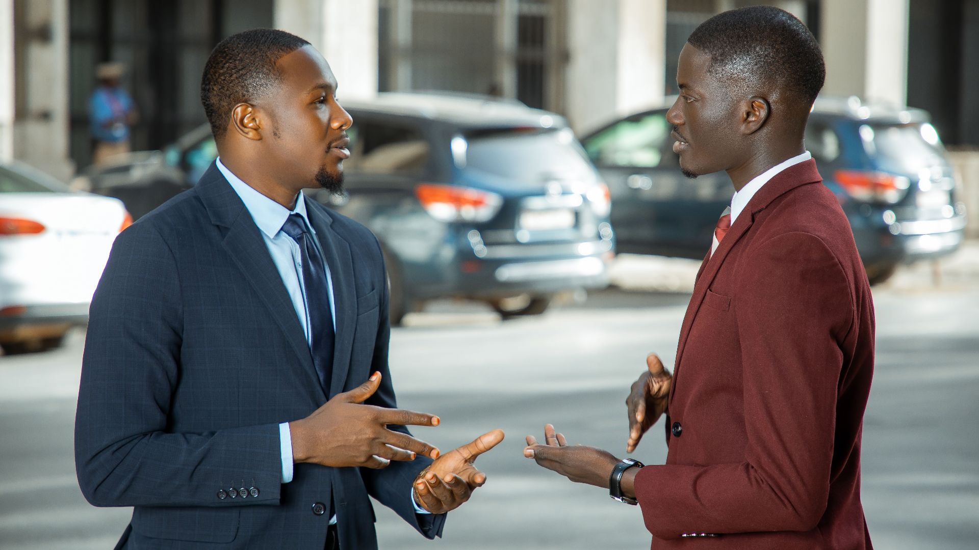 Two African businessmen in formal suits have a discussion on a city street in Dakar, Senegal.
