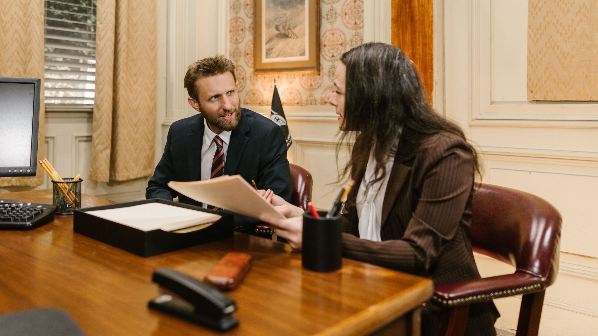 Two professionals engaged in a business discussion in an office setting, reviewing legal documents.