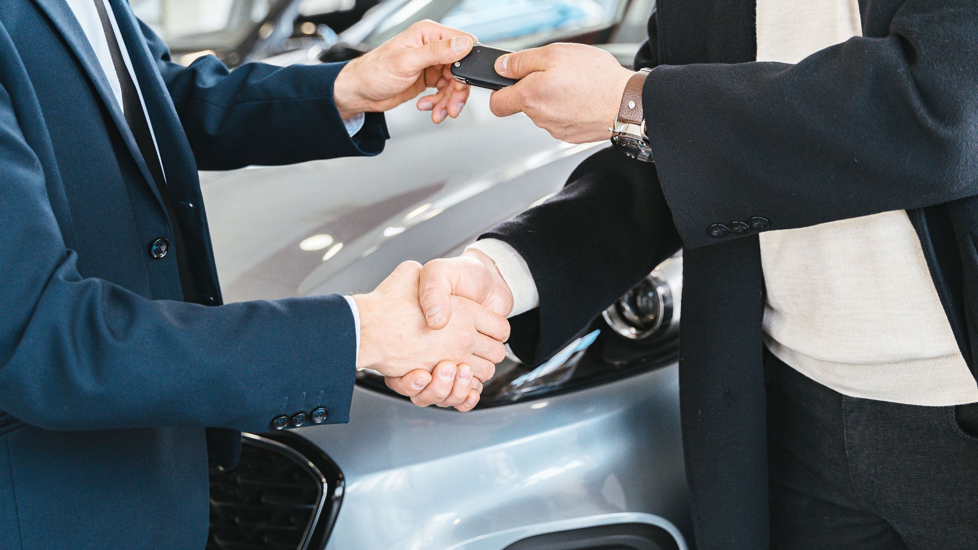 Two businessmen shaking hands and exchanging car keys in a dealership. Symbolizes a successful deal.