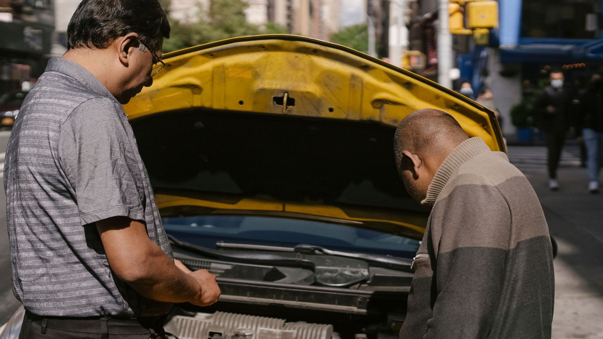 Back view of ethnic man identifying problems in engine system of car under hood standing near driver