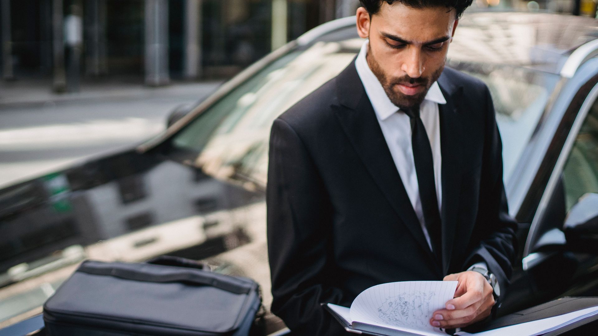 Confident businessman reviewing documents on the street beside a car.