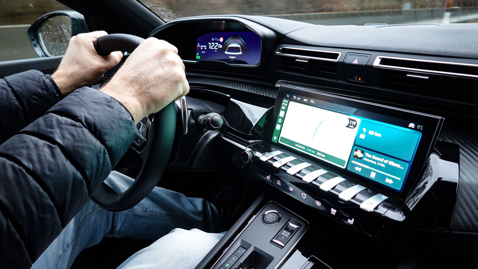 A detailed view of a car's interior with hands on the steering wheel, showcasing modern technology.
