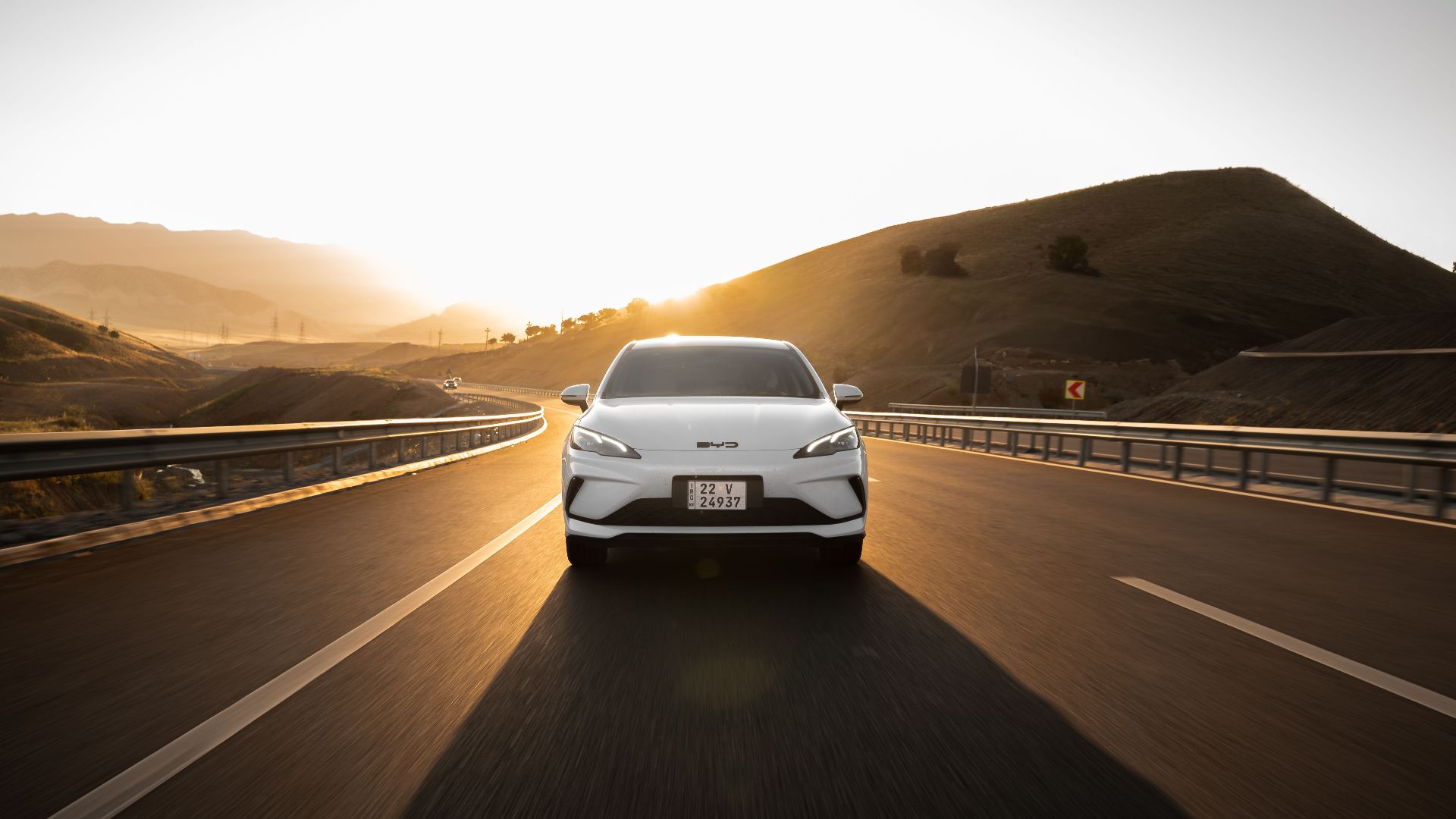 Electric car driving on a scenic highway at sunset, highlighting modern automotive design and sustainable travel.