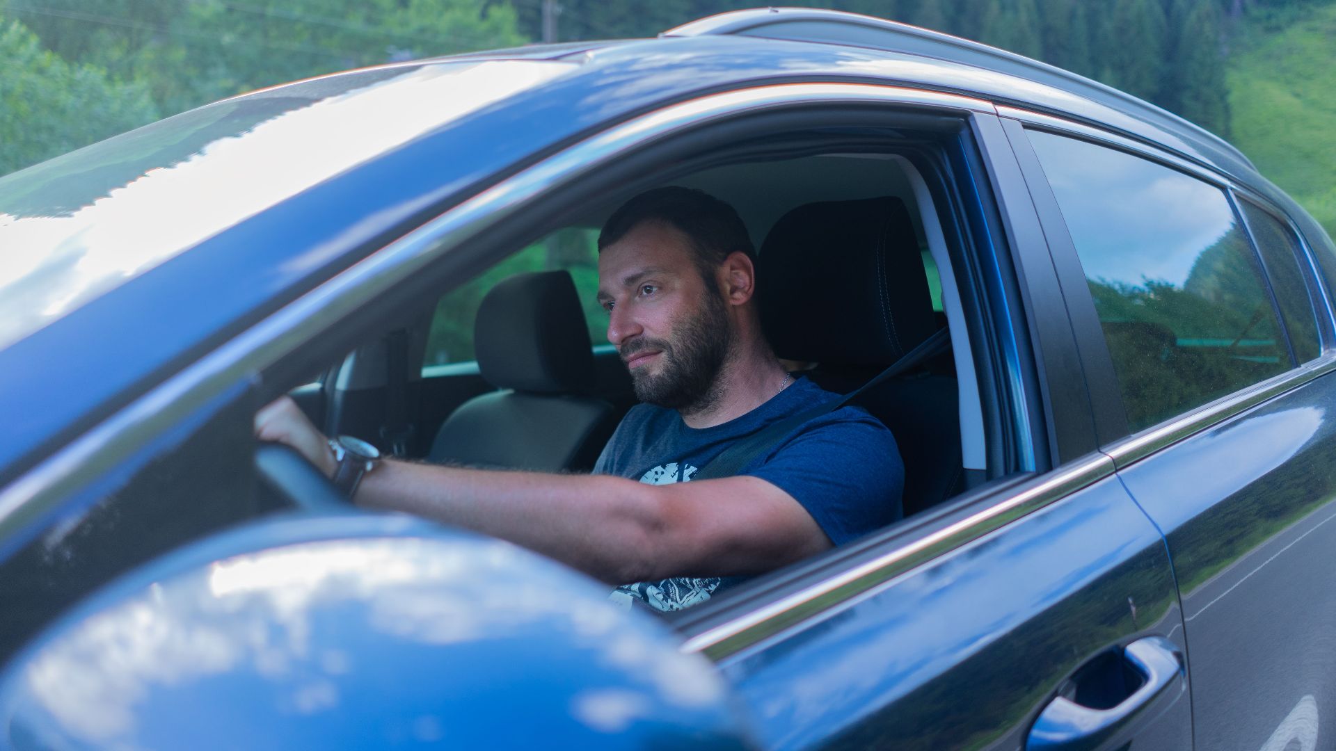 Bearded man enjoying a drive through lush green countryside on a sunny day.