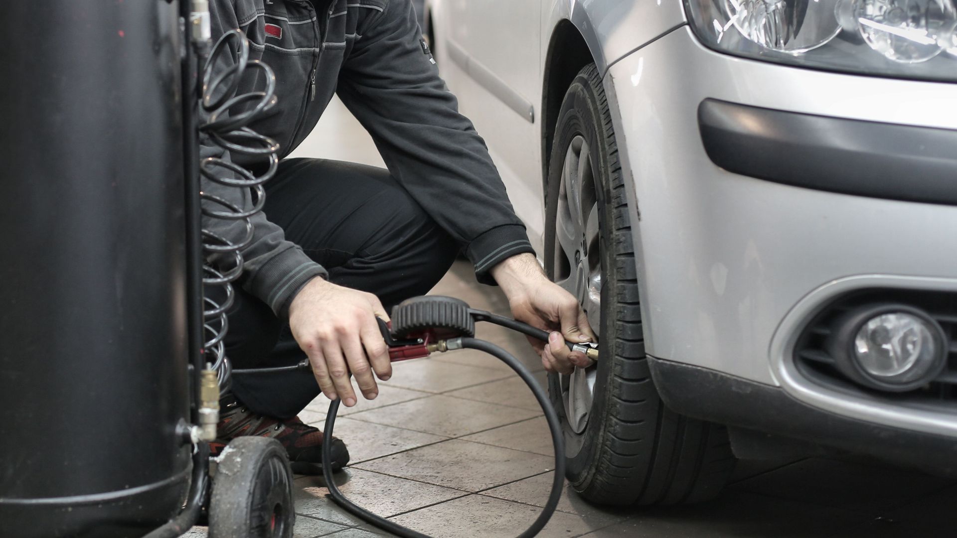 Mechanic inspecting and adjusting tire pressure in an auto repair shop.