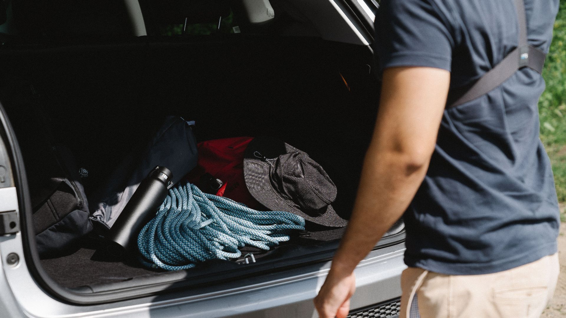 Man organizing camping gear in car trunk, ready for adventure.