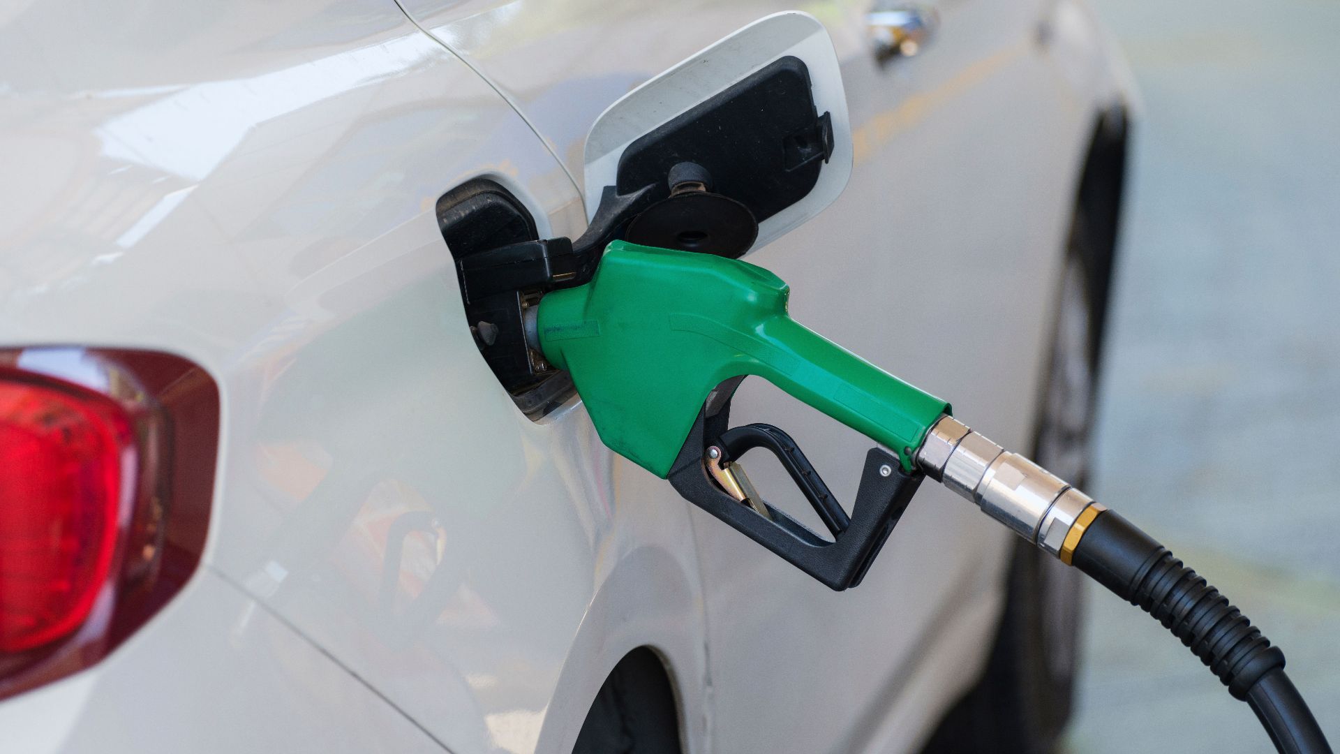 Close-up of a green nozzle refueling a white car at a gas station.