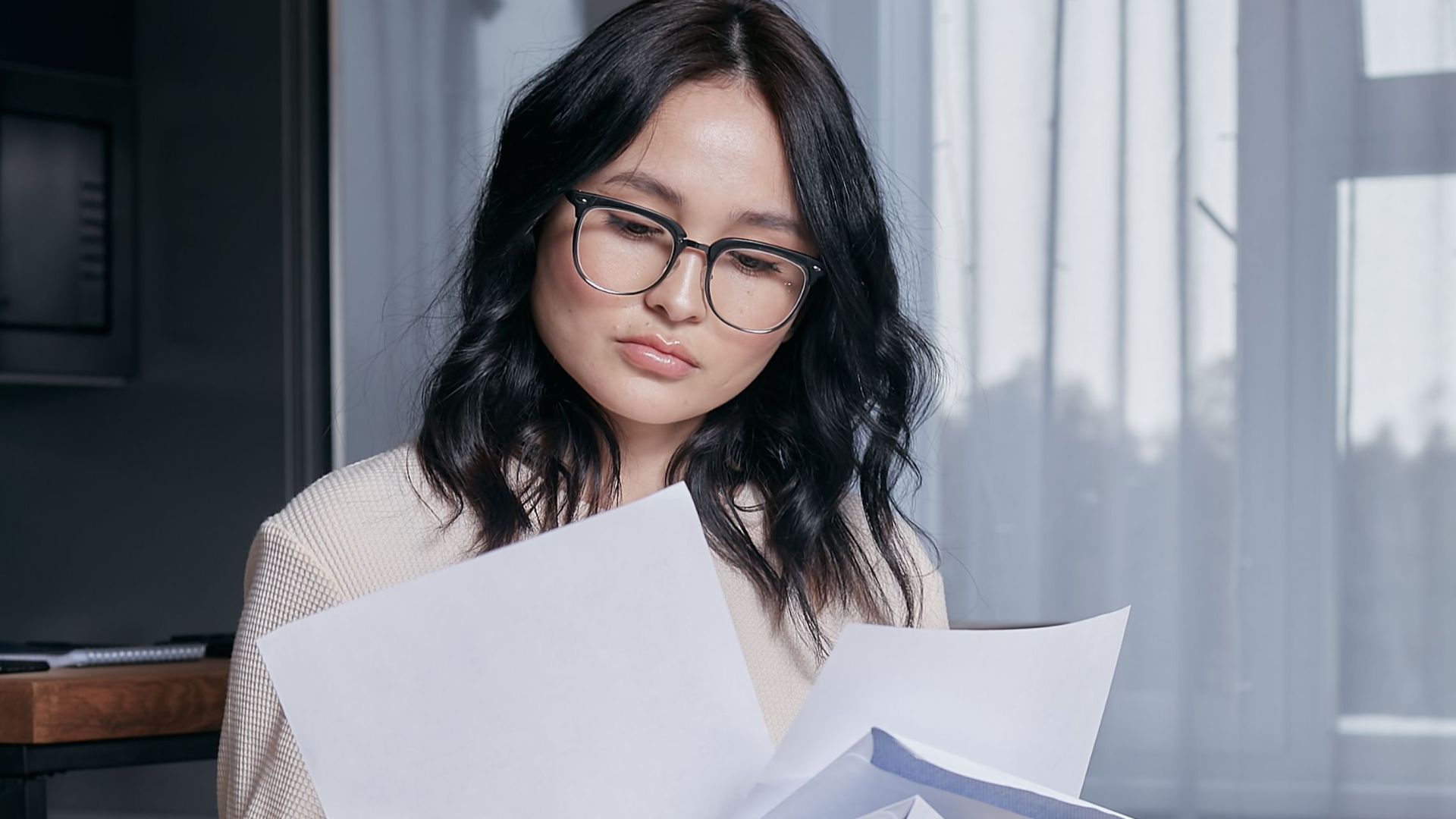 A woman seated indoors carefully reviewing documents, initiating thoughtful analysis.