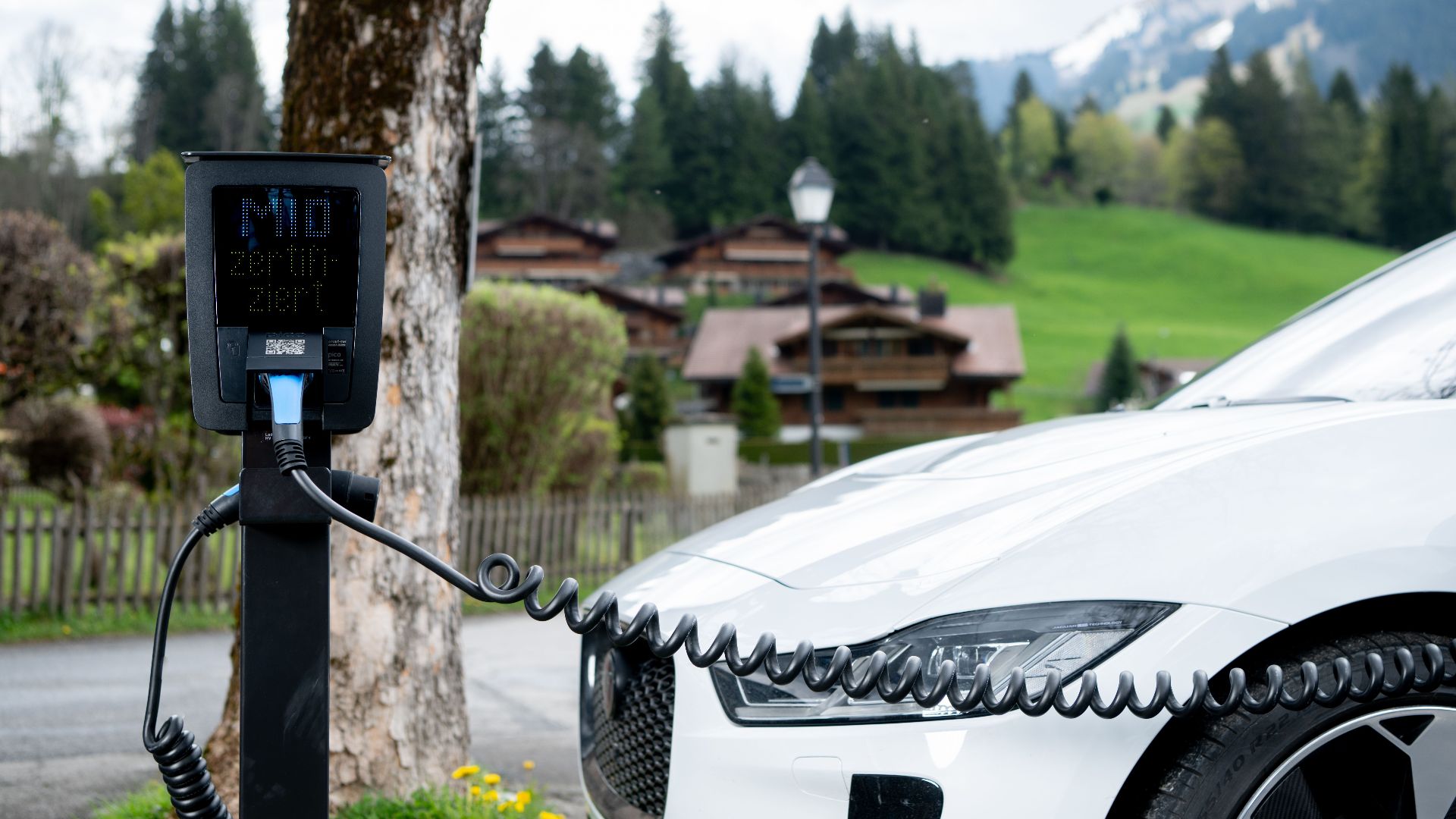 Electric car charging at a station in a picturesque mountain village, promoting sustainable transportation.