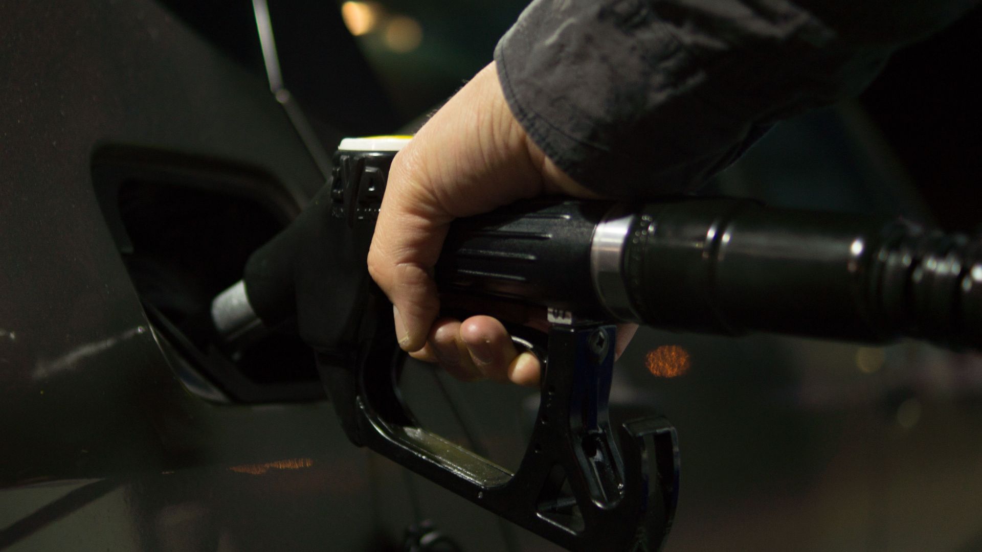 Close-up of a person refueling a car at a gas pump during night.