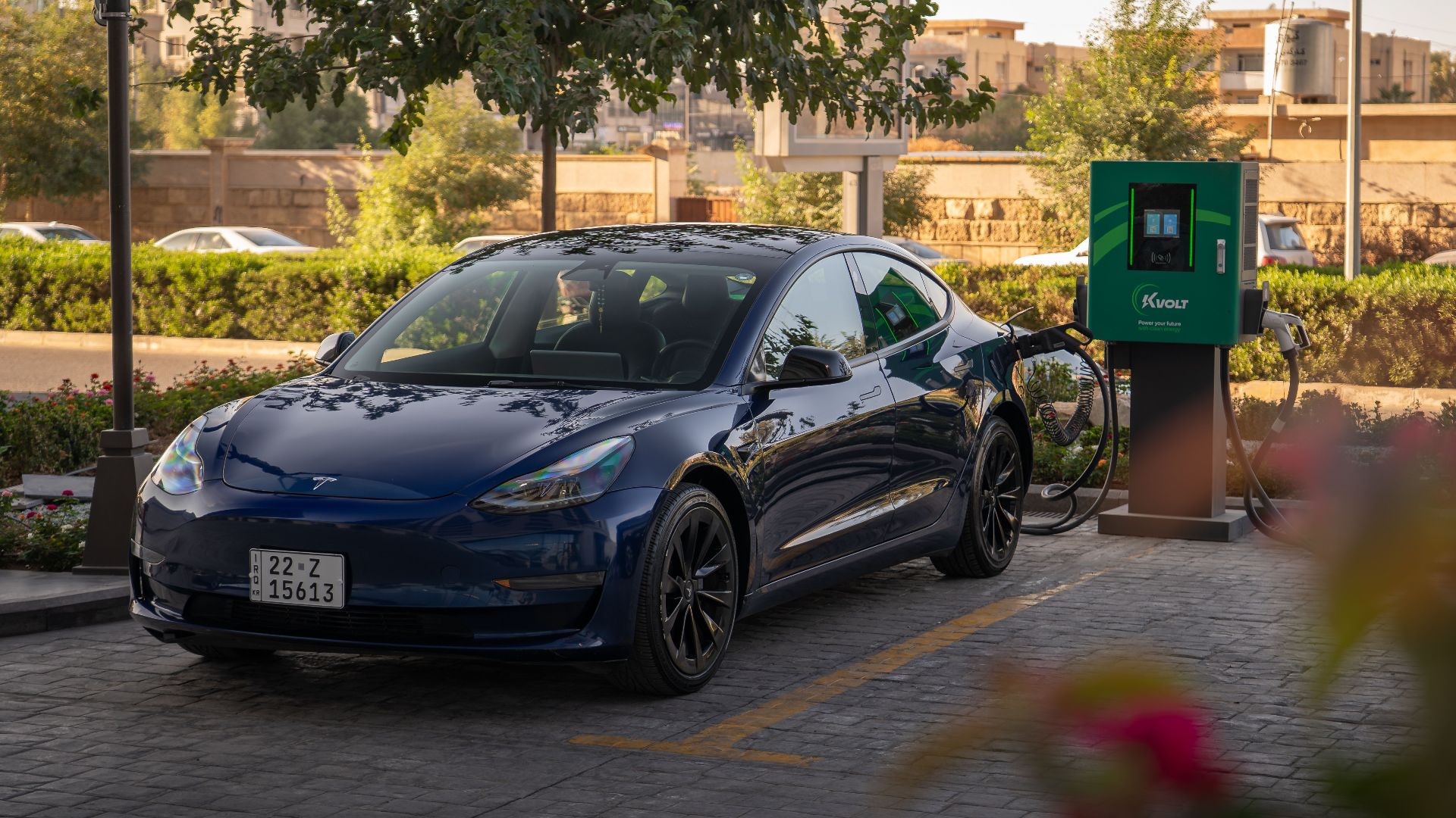 Tesla Model 3 charging at an urban electric vehicle station during daytime.