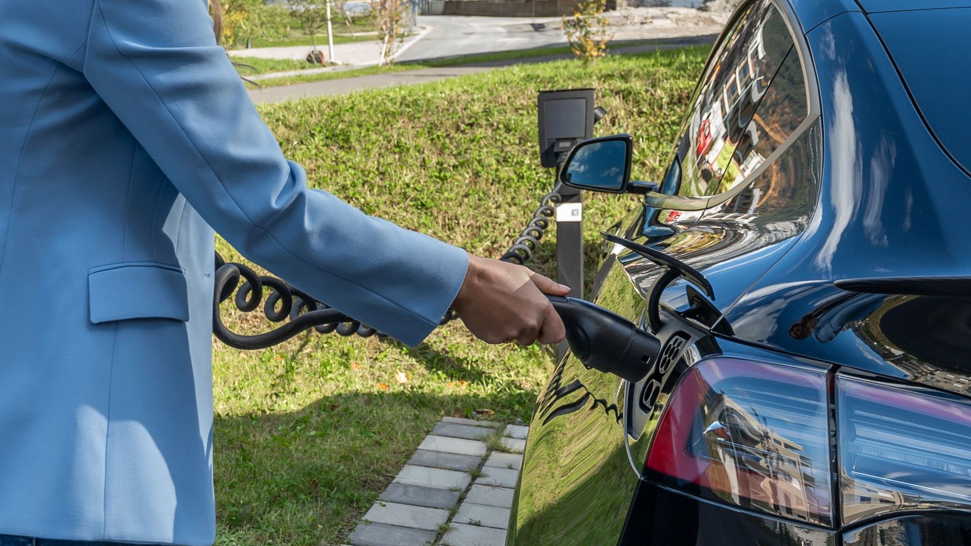 Person connecting an electric car to a charging station outdoors, showcasing green energy transition.